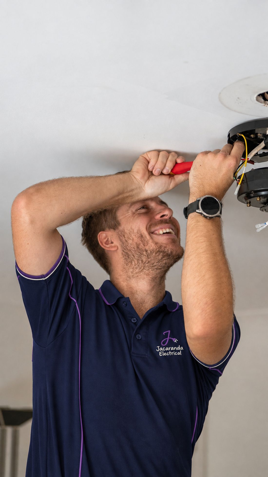 Jack Beath in a Jacaranda Electrical polo, wiring a ceiling light fitting